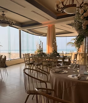 A large room with tables and chairs and a large window overlooking the ocean.