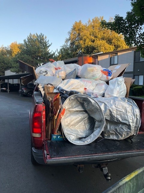 Pickup truck bed piled high with bagged and bundled trash bags in a parking lot at dusk