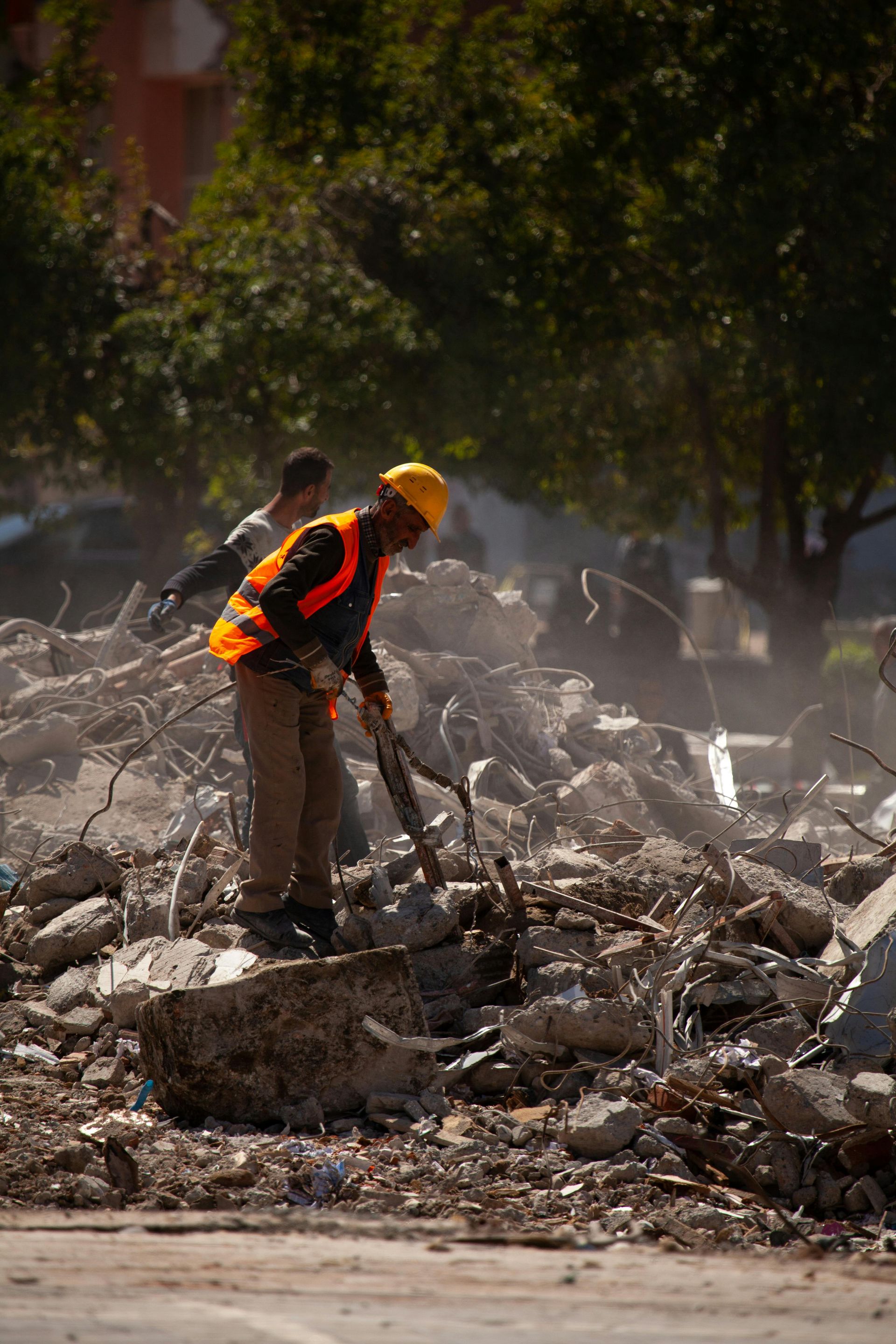 Construction worker in orange safety vest and yellow hard hat clearing rubble at a demolition site.
