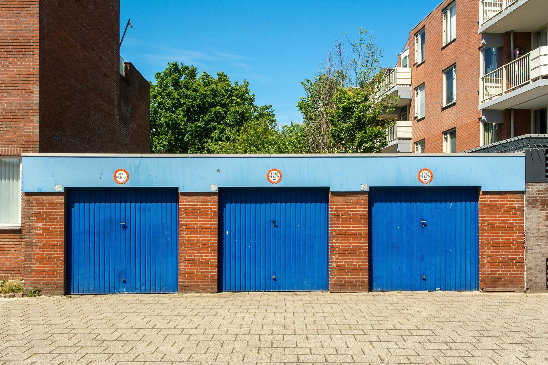 Three blue garage doors in a brick building under a clear sky.