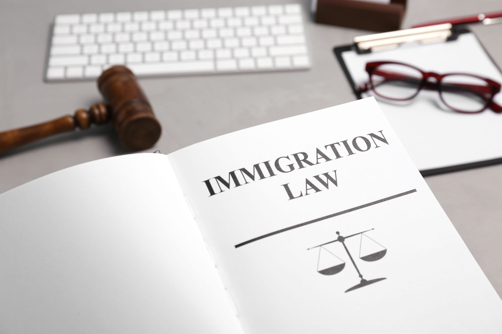 Open book labeled “Immigration Law” with judge’s gavel, keyboard, and glasses on desk