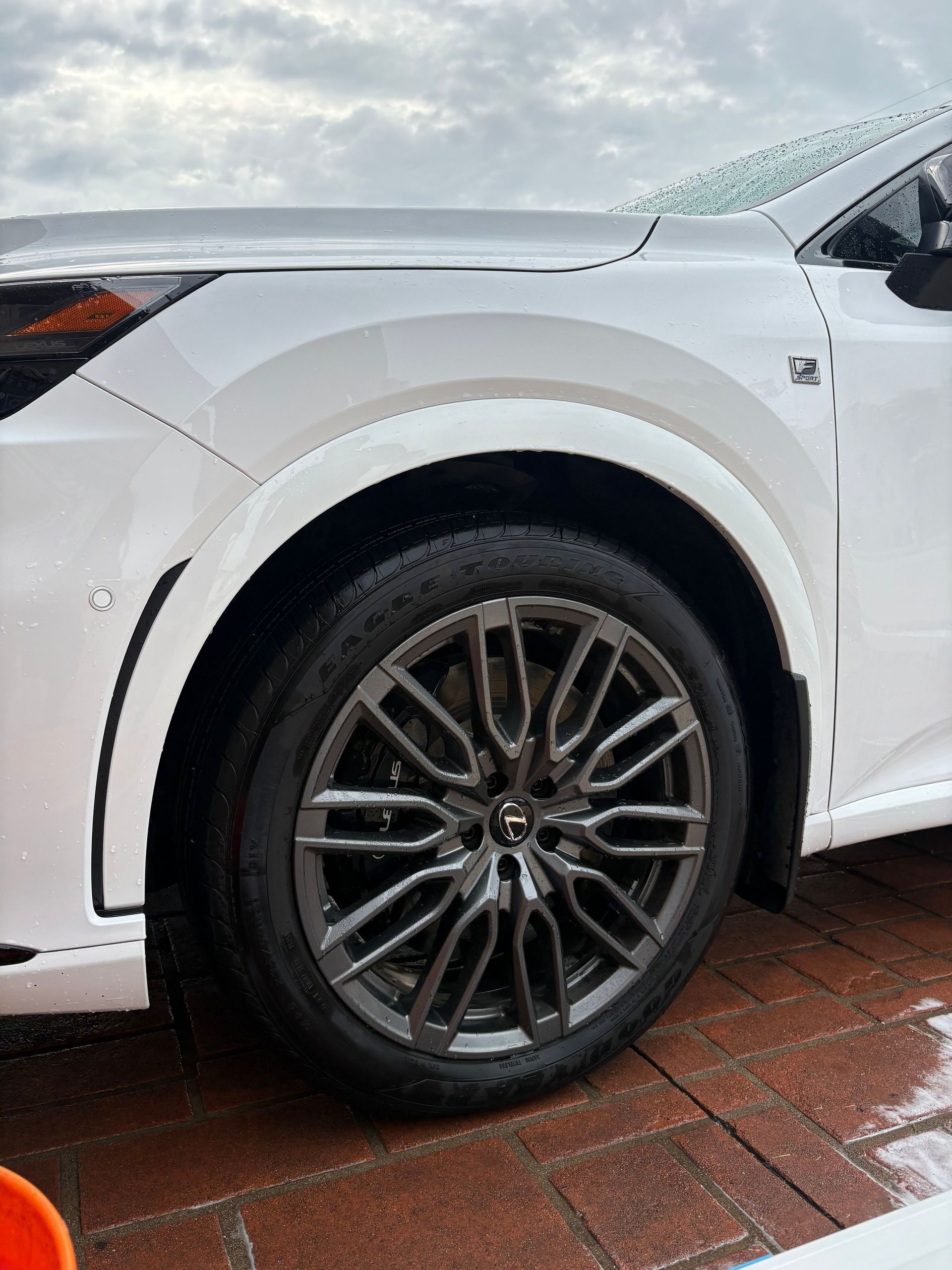 Front wheel and fender of a white car on wet pavement, showing a dark alloy rim.