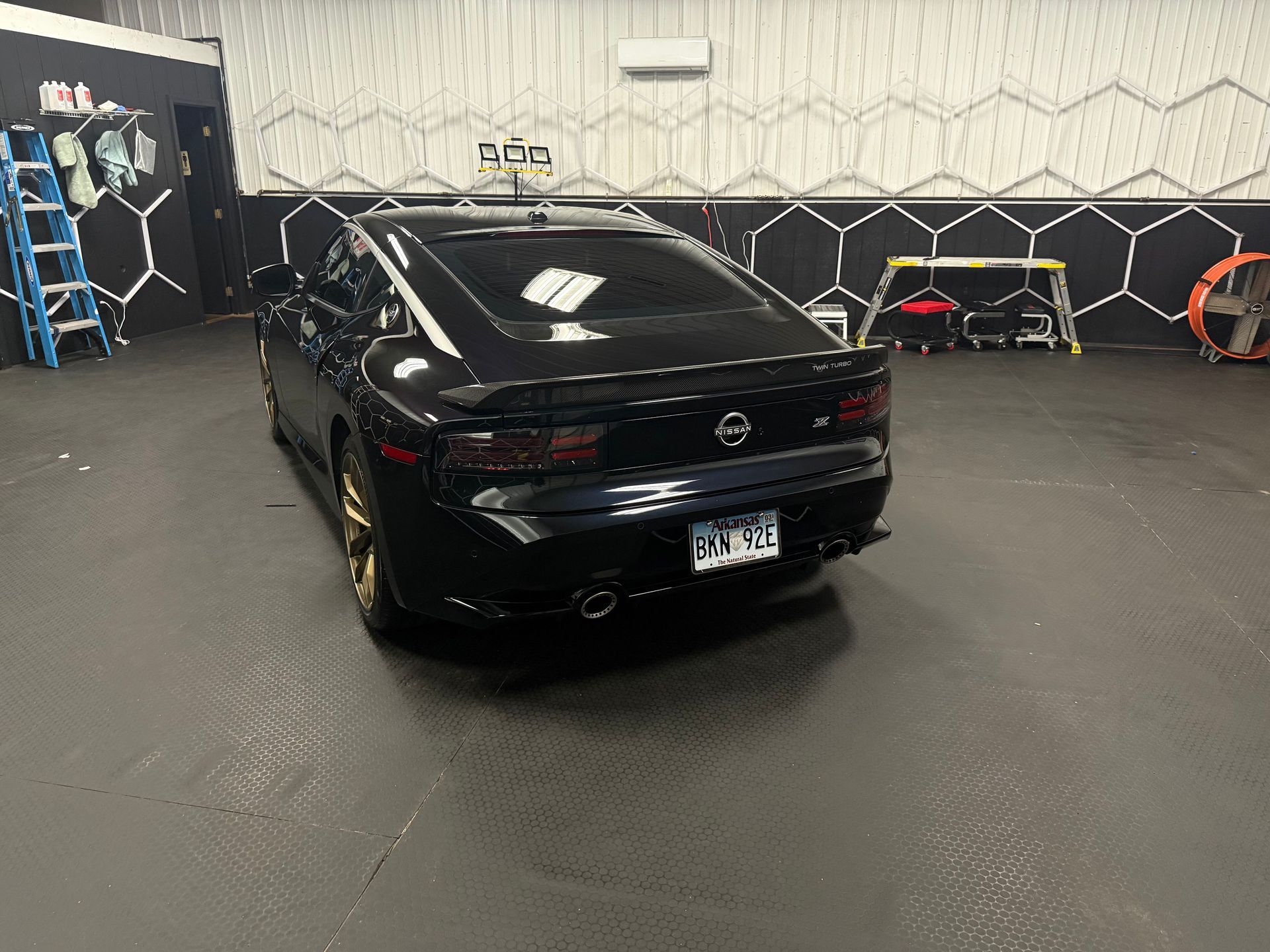 Black sports car parked indoors in a garage with a patterned wall and equipment in the background