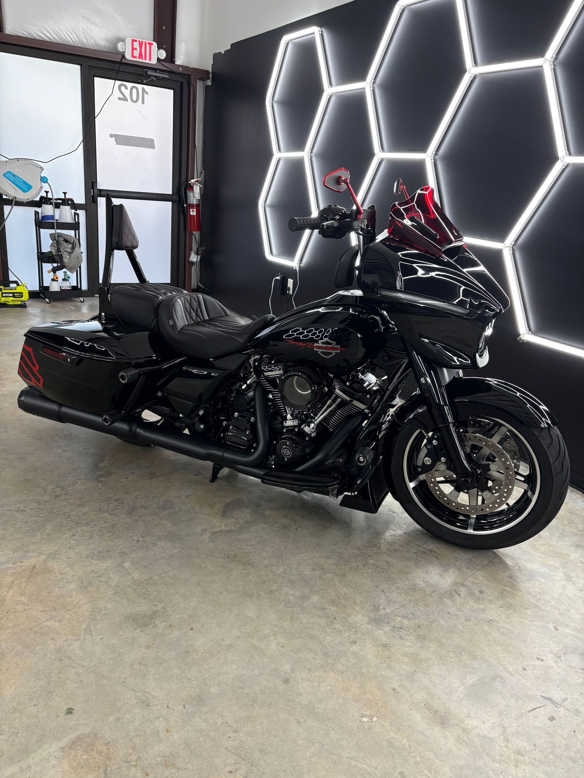 Black motorcycle in a showroom with geometric LED wall lights and a concrete floor.
