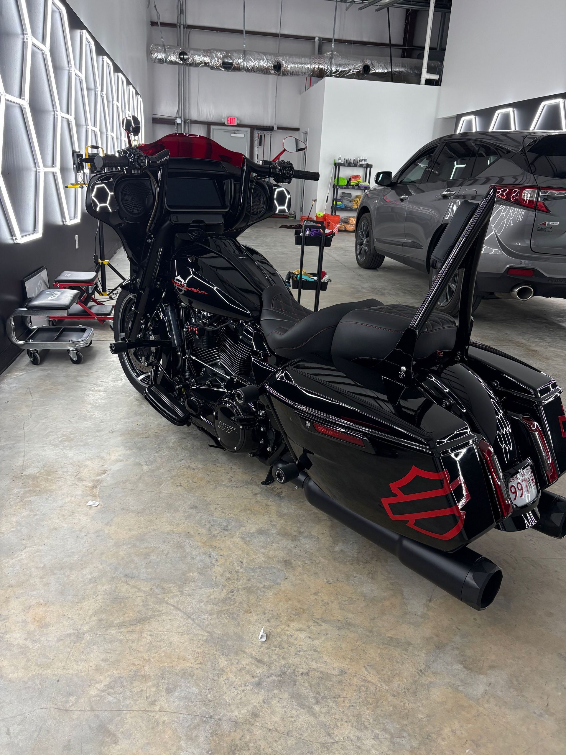 Black touring motorcycle in a garage, with a car parked beside it and tools along the wall.