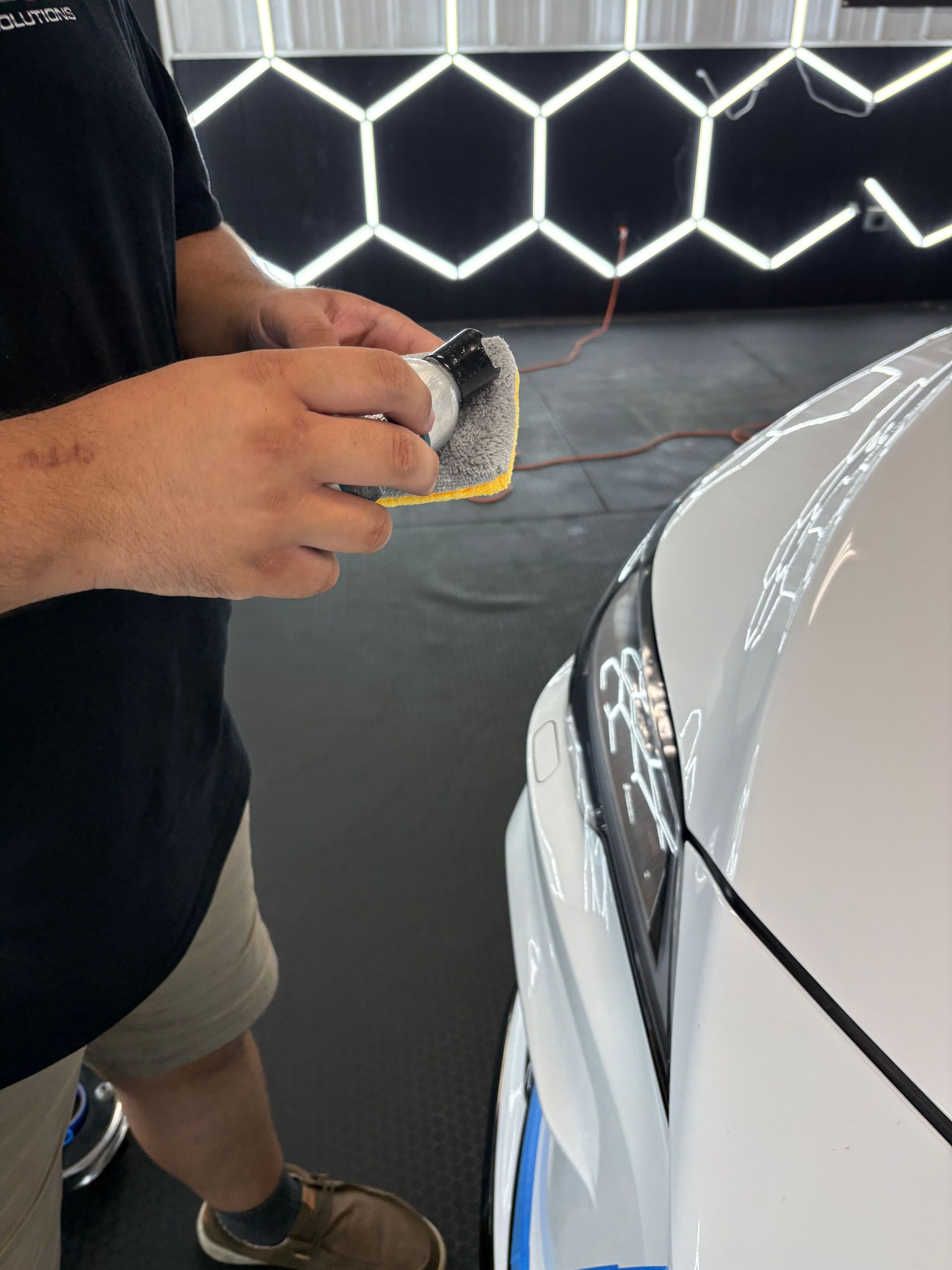 Person using a cloth to clean a white car front near a neon-lit wall