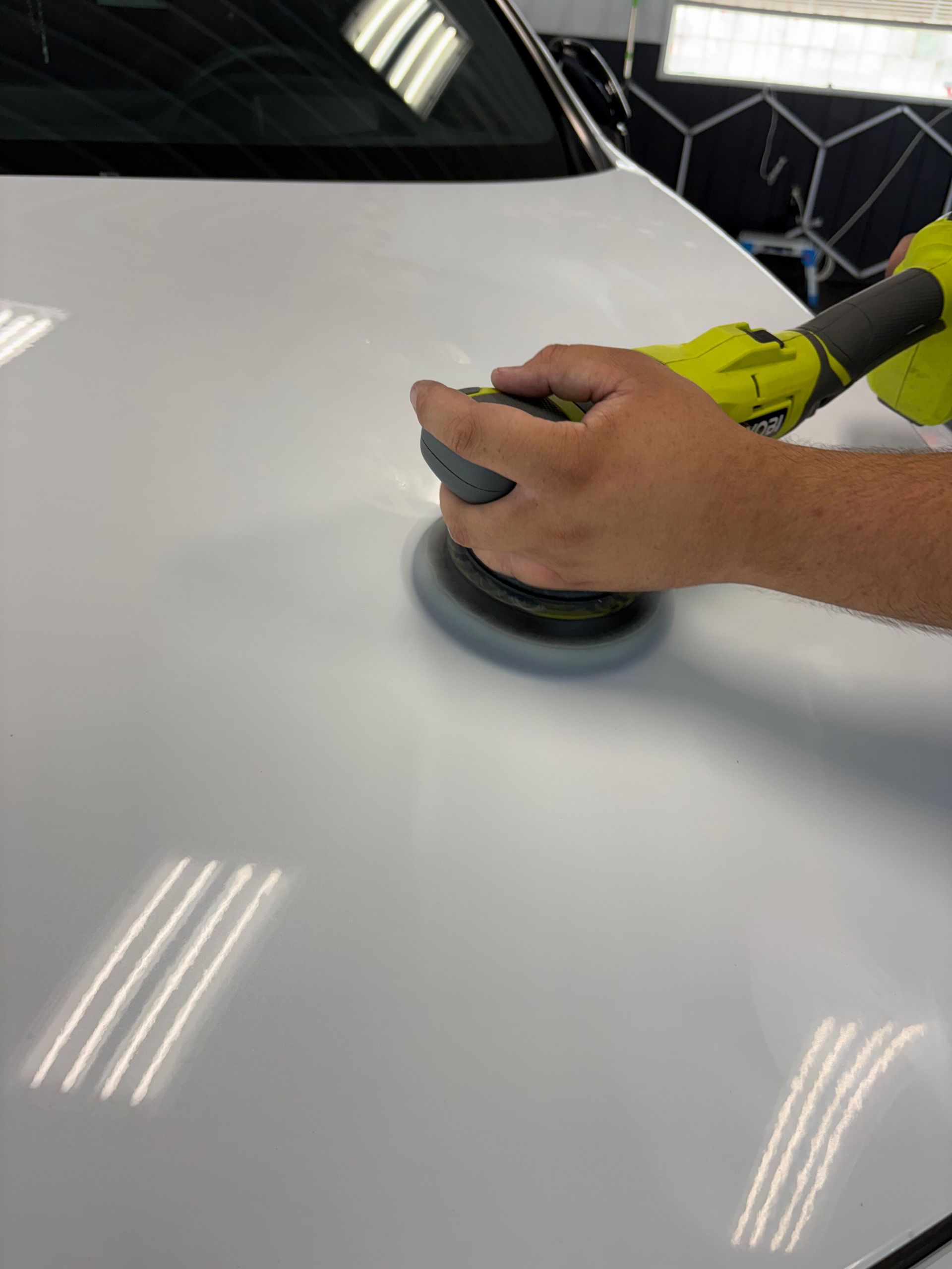 Hand using a polisher on a white car hood in a workshop