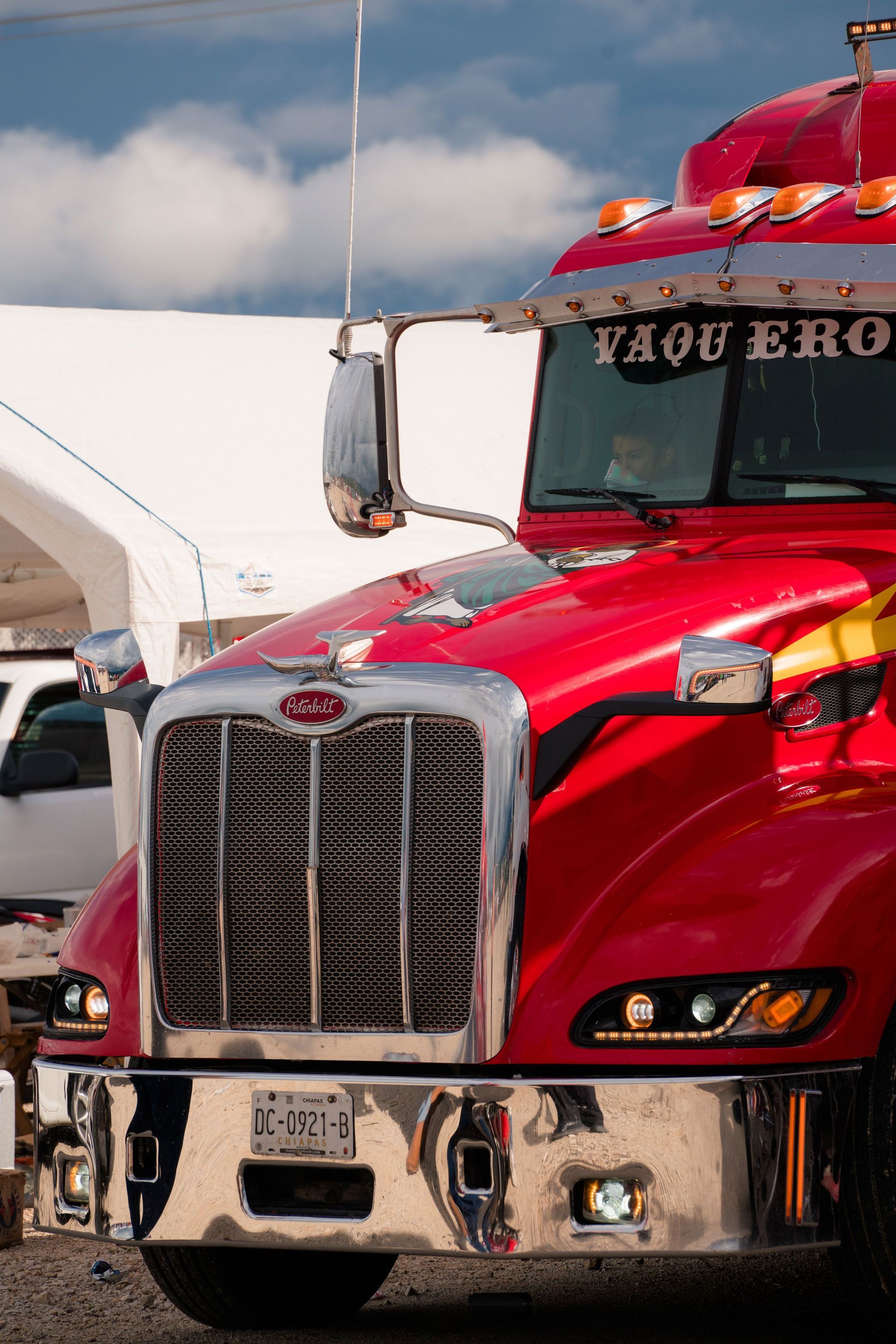 Red semi truck with chrome grille parked outdoors under a blue sky.