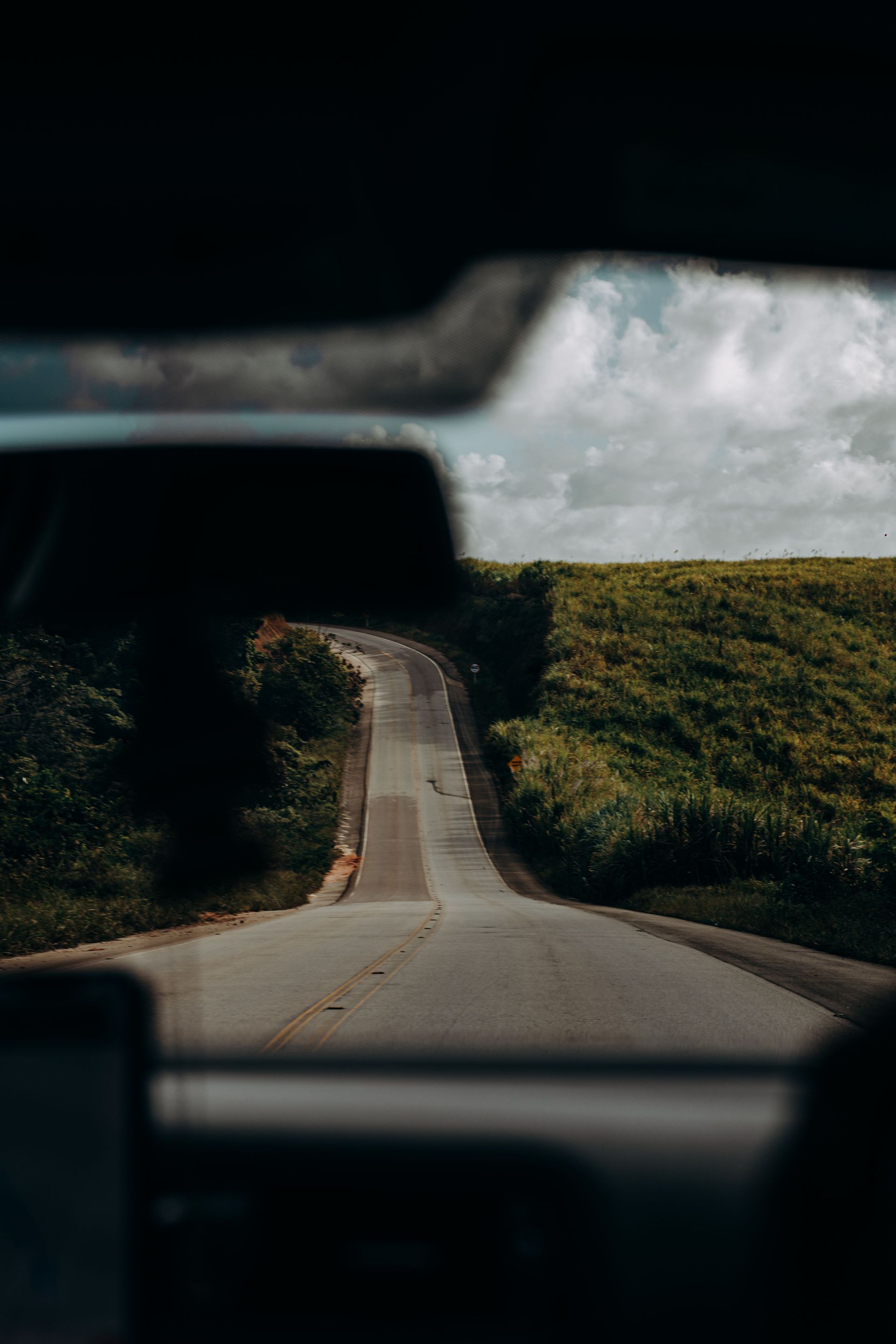 A road stretching between green hills, seen through a car windshield with a blurred dashboard in the foreground.