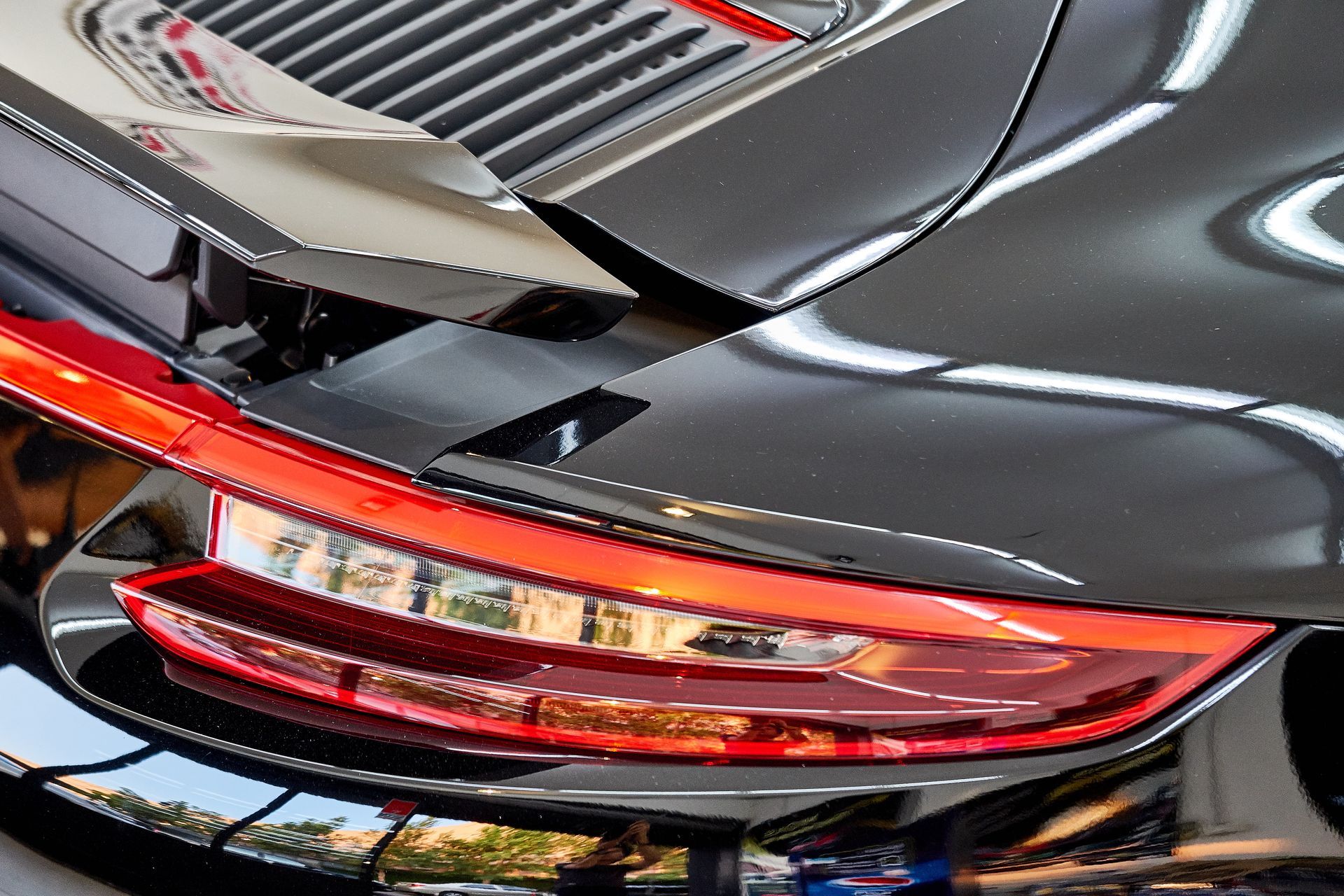 Close-up of a black sports car’s rear taillight and trunk grille with red accents