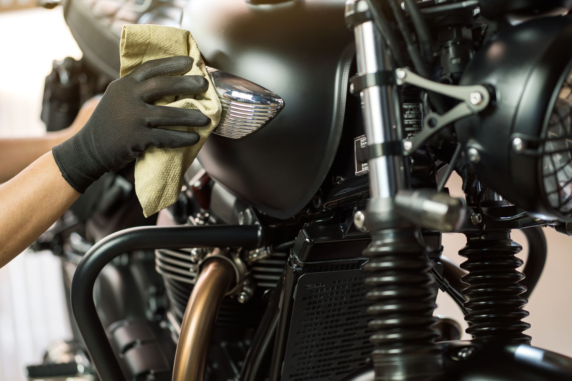 Gloved hand wiping a black motorcycle tank with a cloth during cleaning