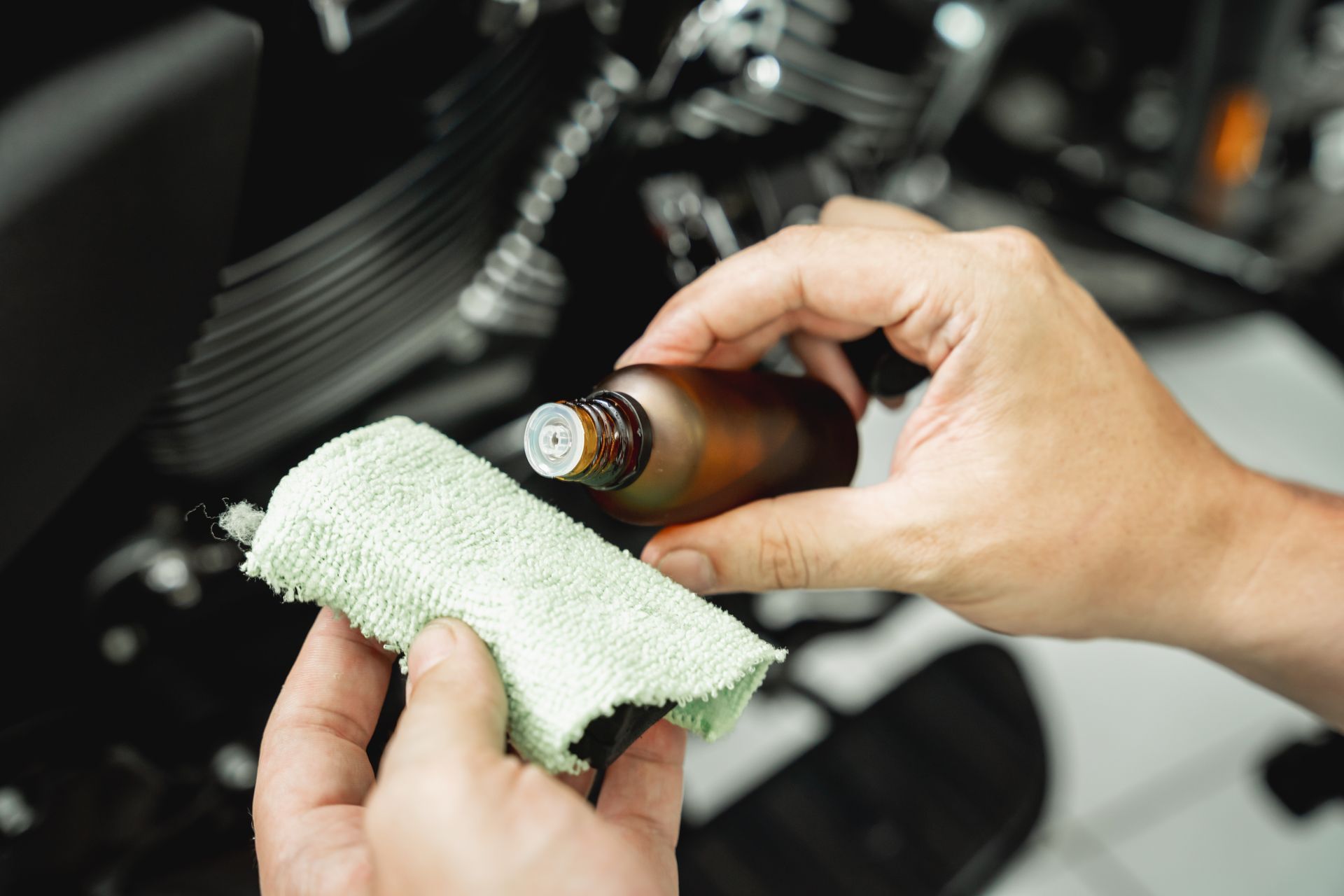 Hands holding a brown bottle and a microfiber cloth, cleaning a car interior surface.