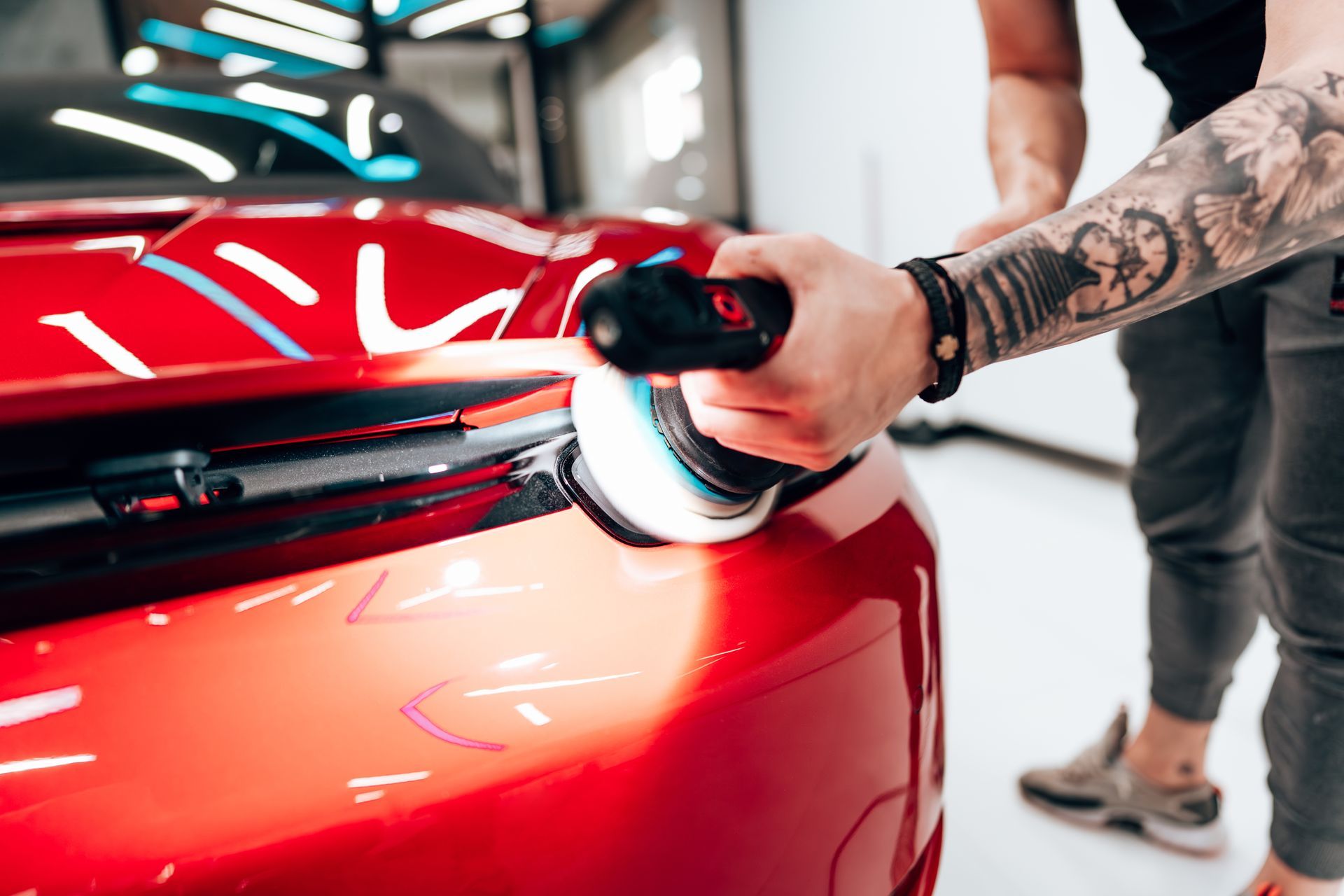 Person polishing a red sports car with a buffing machine in a bright garage