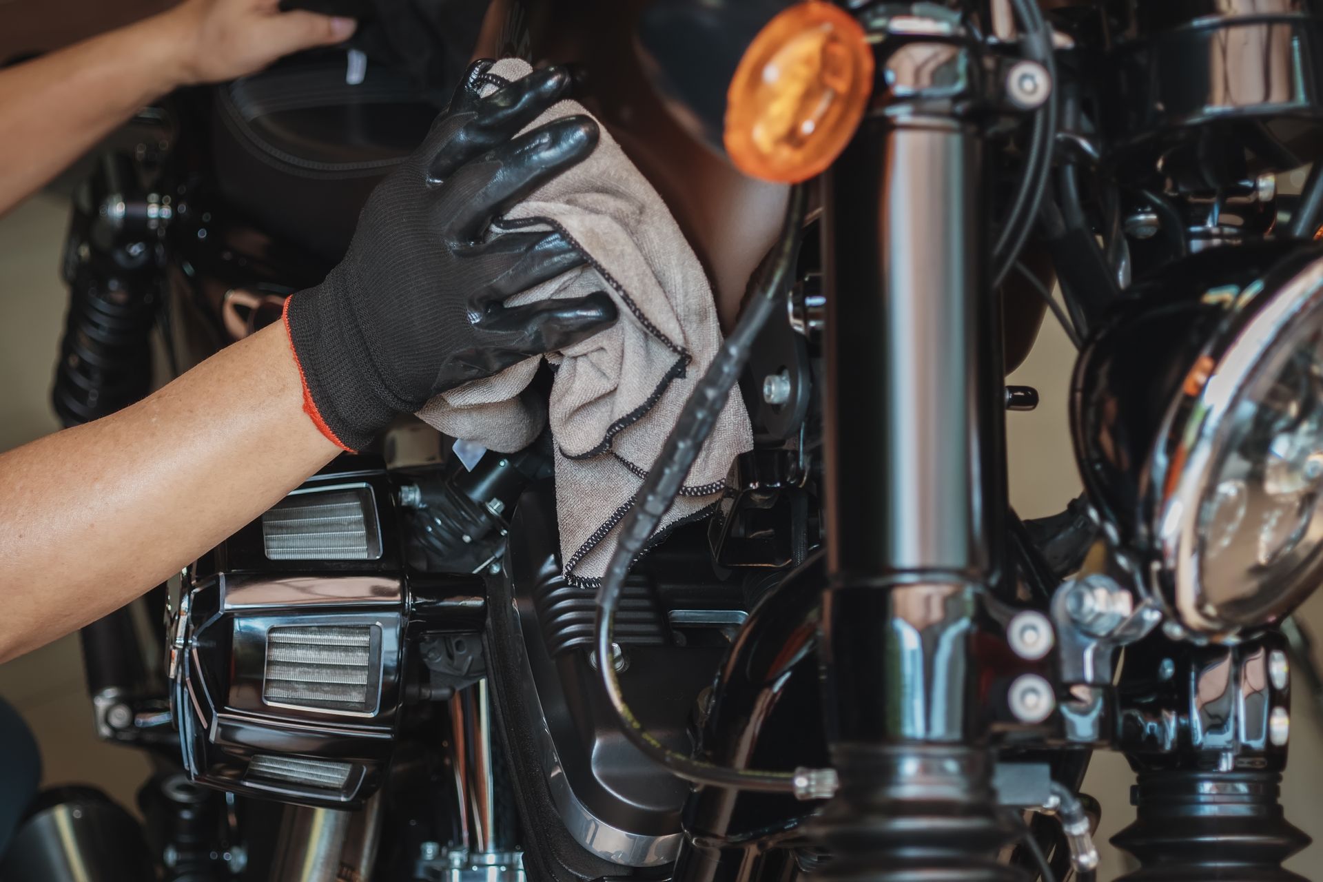 Gloved hand wiping a black motorcycle engine with a cloth