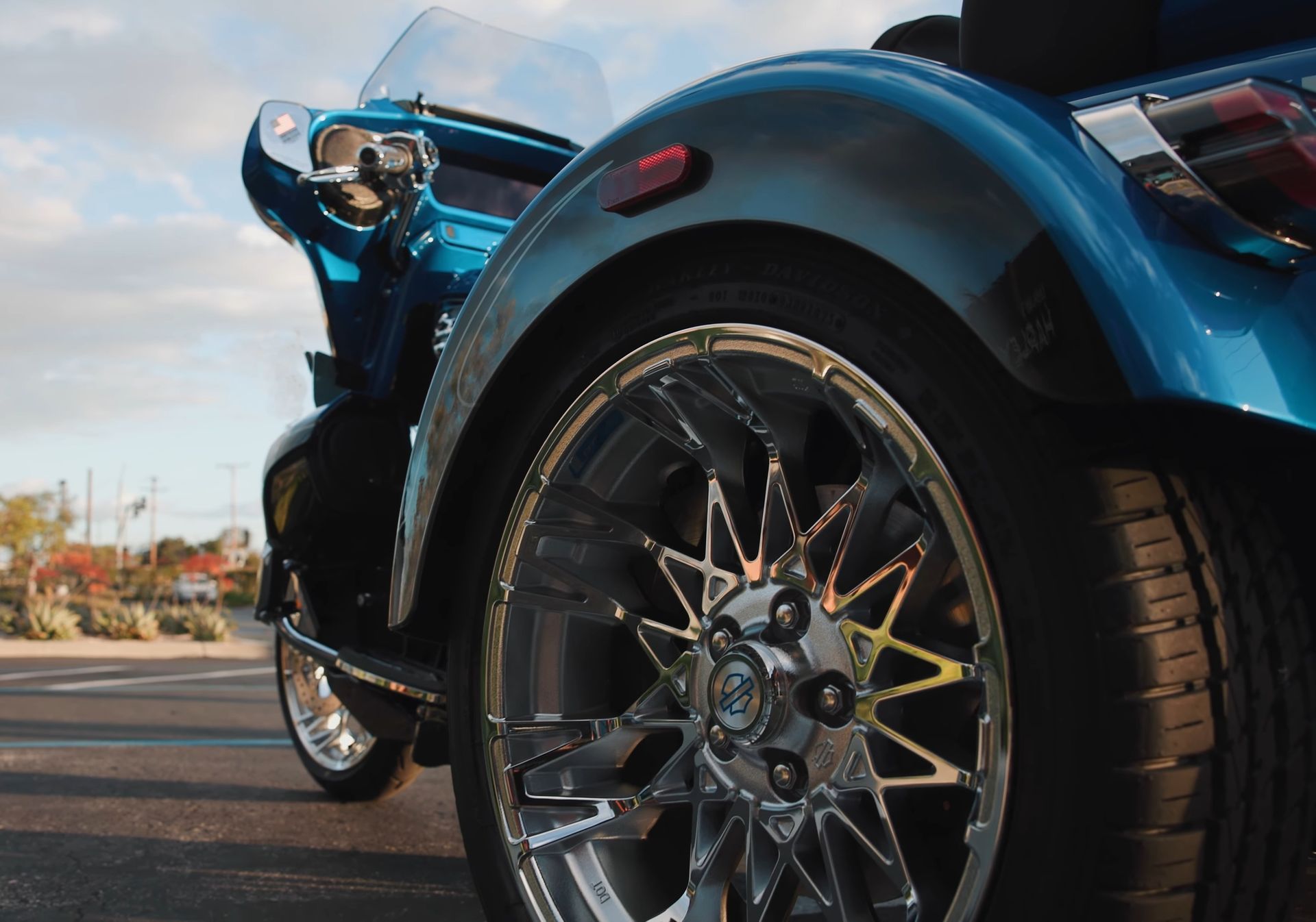 Close-up of a blue sports car’s chrome front wheel parked outdoors at sunset