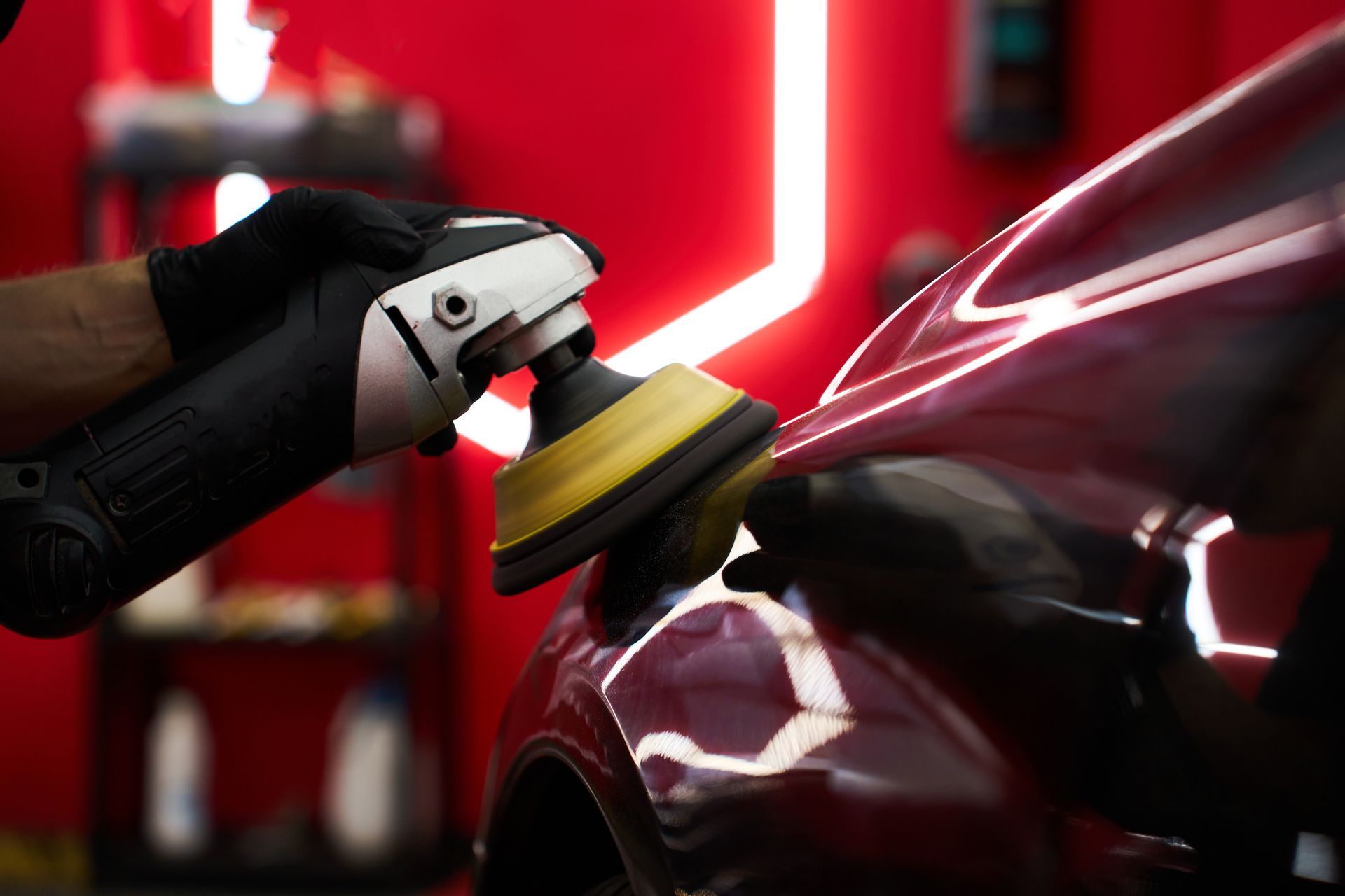 Person polishing a red car body with a buffer in a workshop