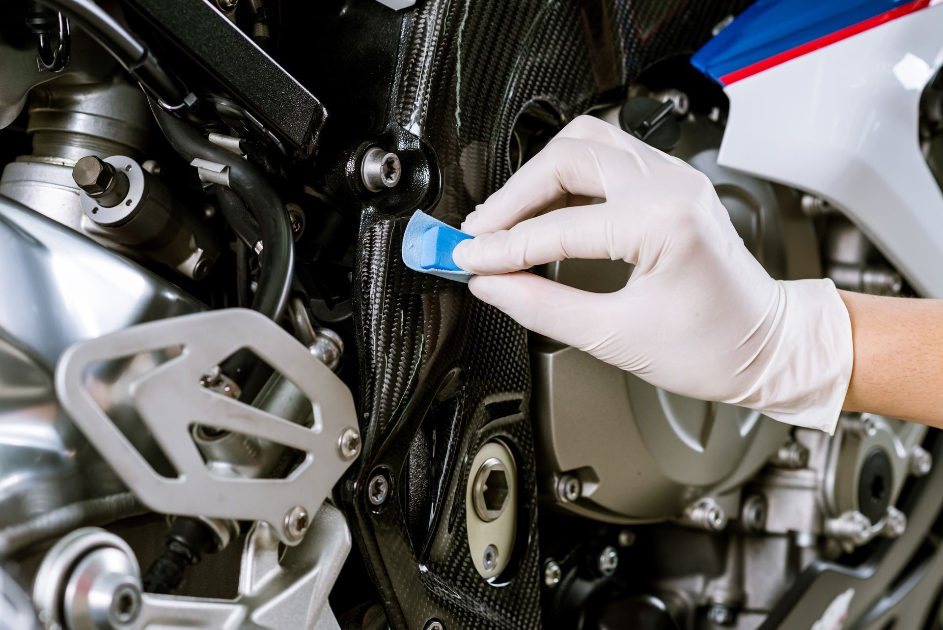 Gloved hand inspecting a motorcycle engine with a blue tool in a workshop