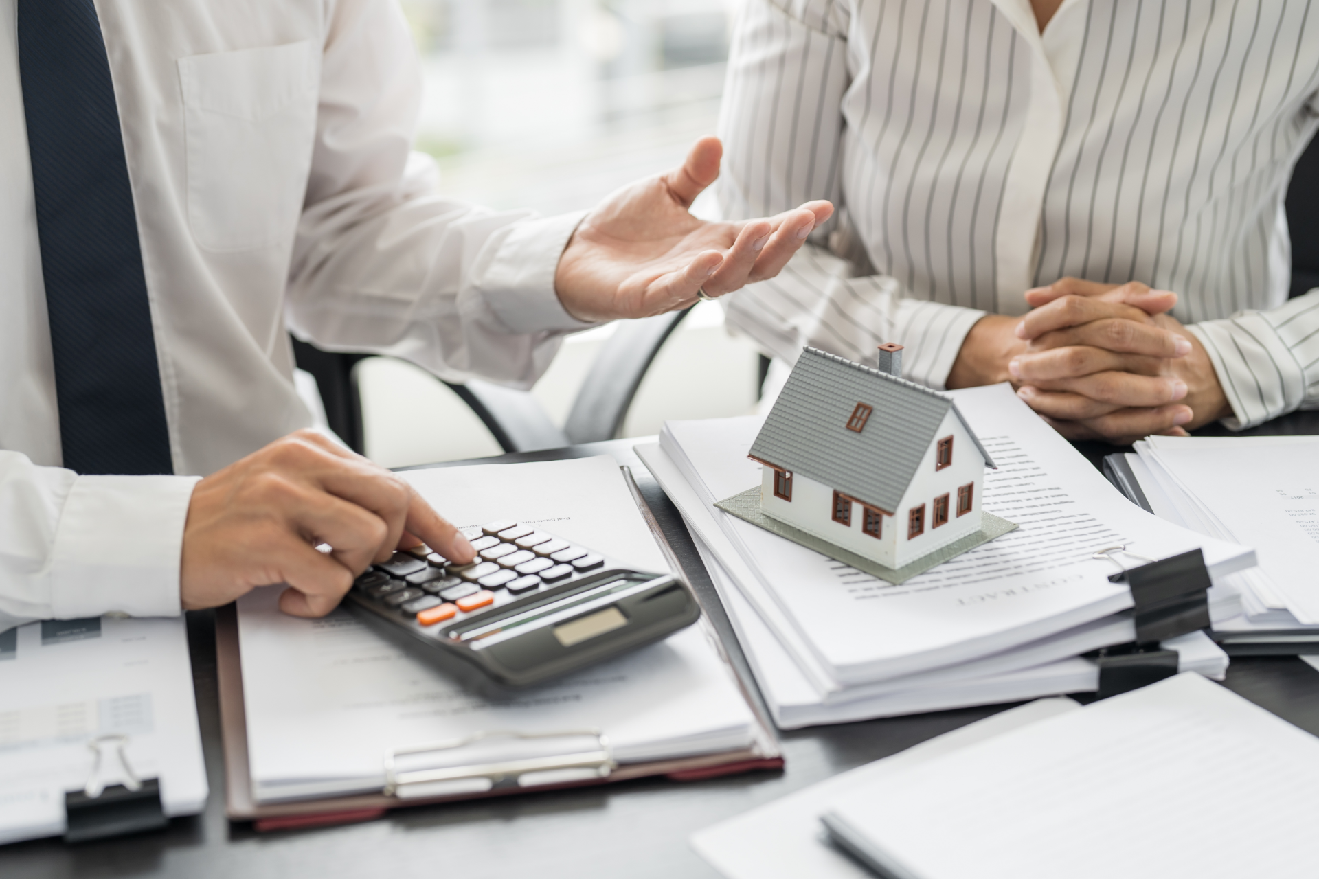 Real estate agent explaining mortgage options to a client, using a calculator and model house.