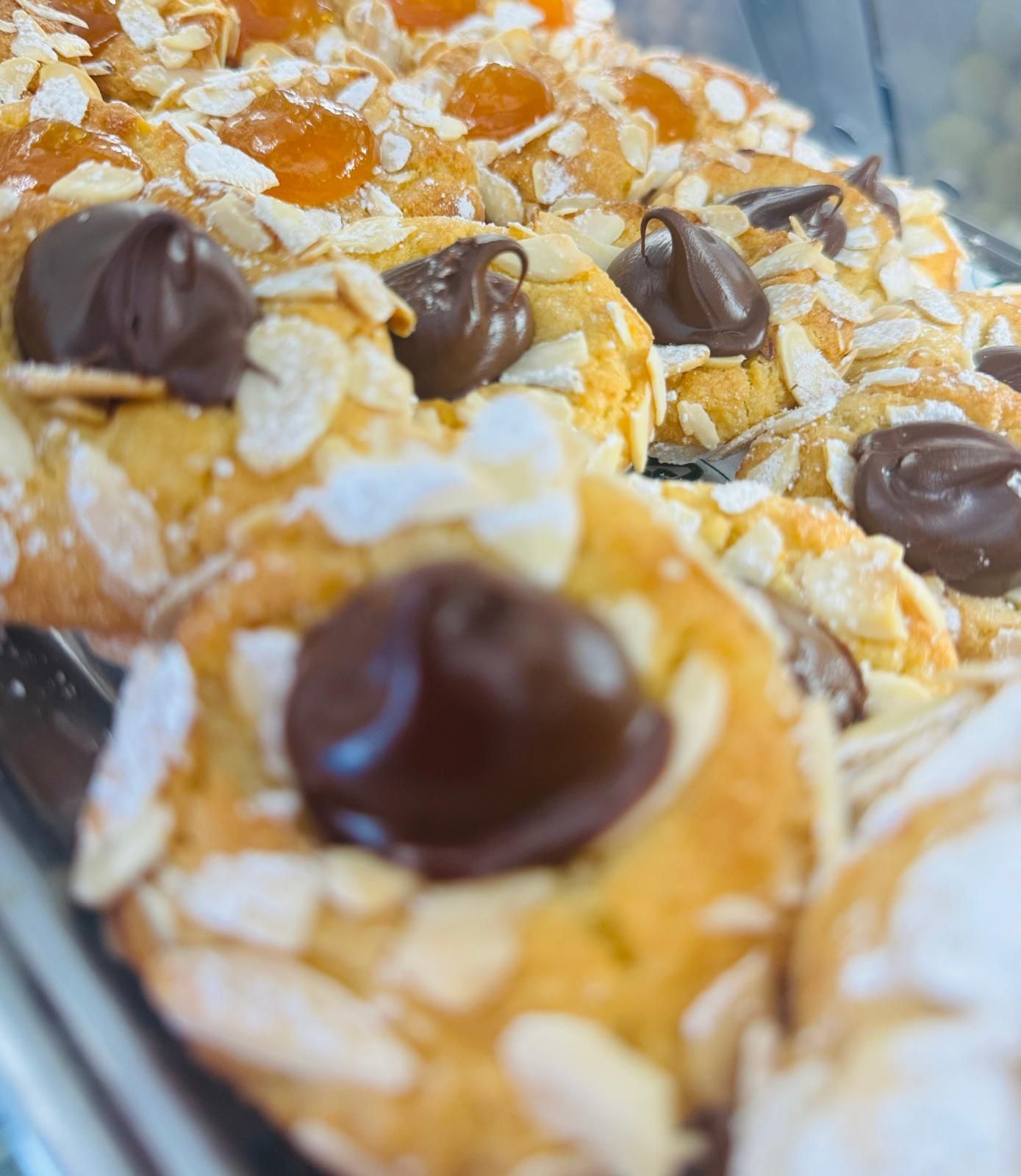 Biscotti ricoperti di mandorle, cioccolato e albicocche esposti in una vetrina.