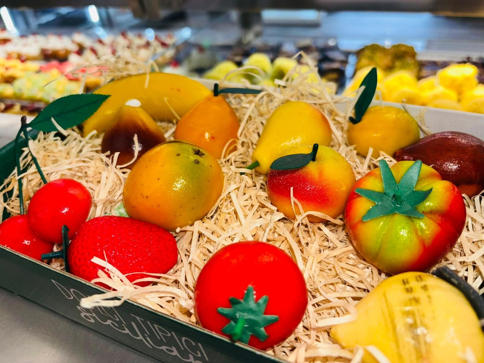 Assortimento di frutta in marzapane in una scatola decorativa con cannuccia. Include limoni, pomodori, mango, pere e mele.