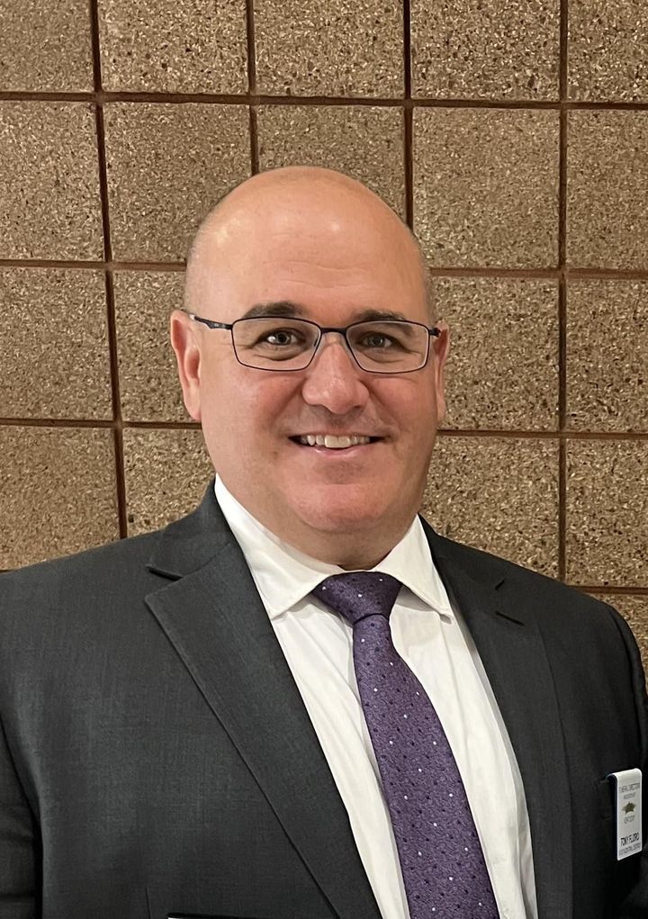 Man in suit and purple tie smiling in front of a tan tiled wall