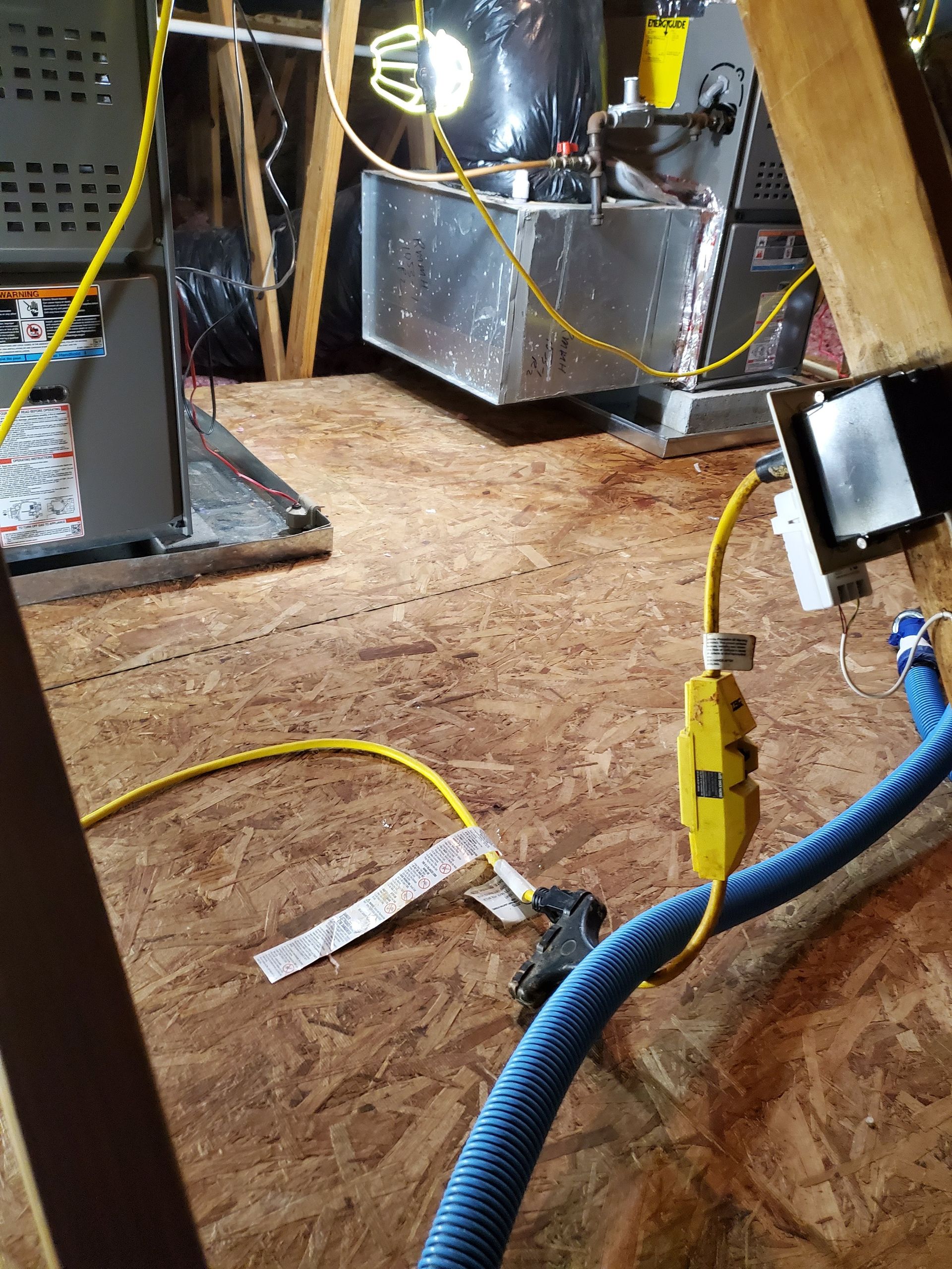 A blue hose is connected to a yellow cord in an attic