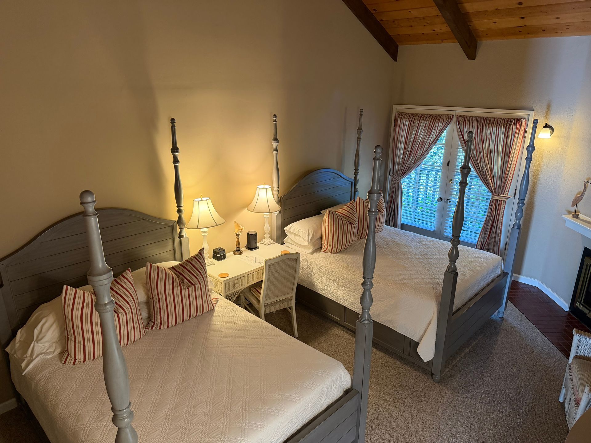 Two gray four-poster beds in a bedroom with a desk, window, and fireplace.