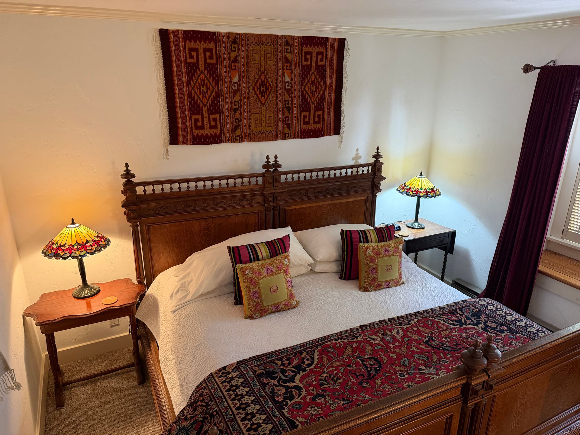 Bedroom with antique wooden bed, lamps, rug, and patterned wall hanging.
