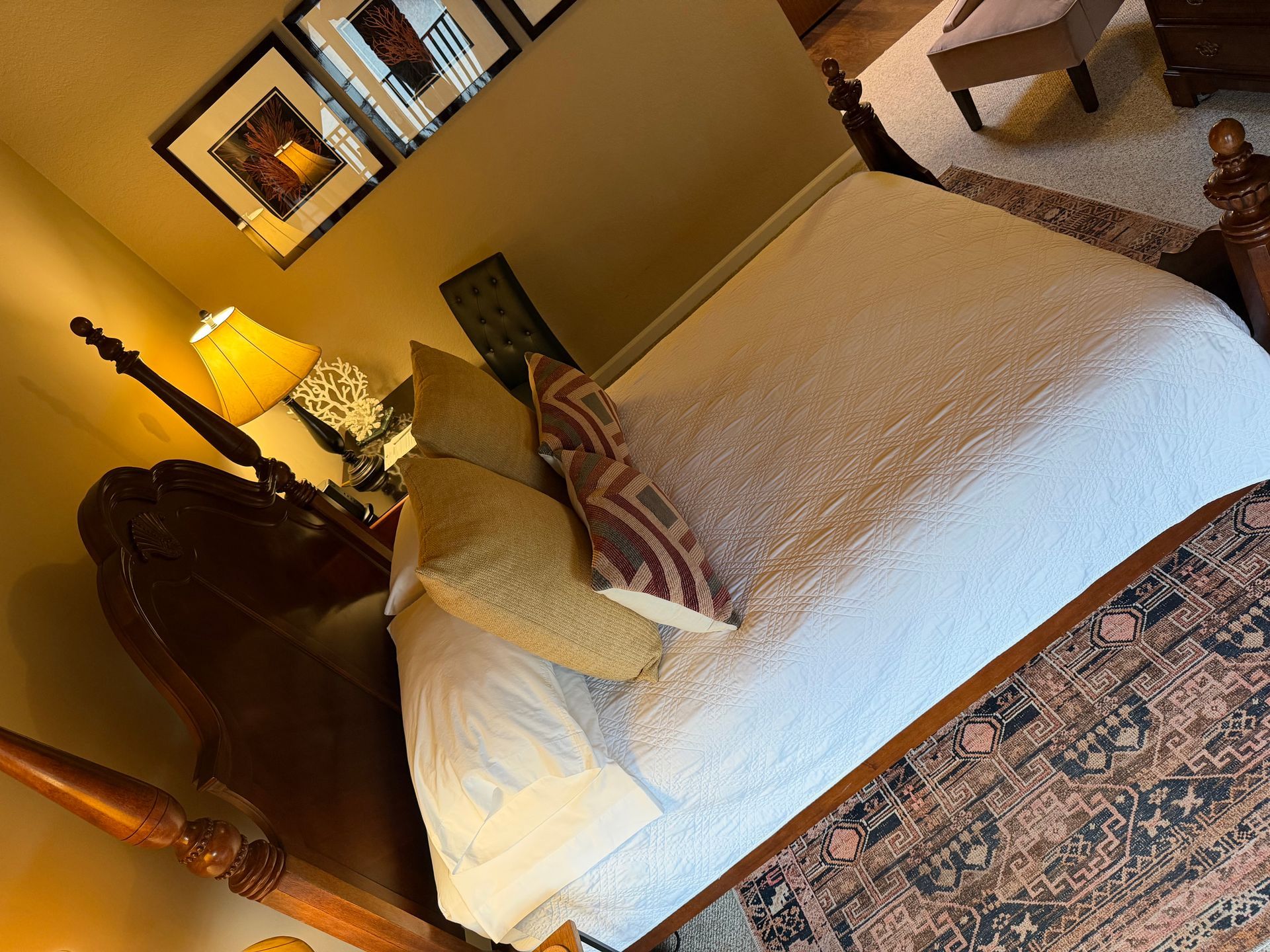 Bedroom with a wooden four-poster bed, white bedding, pillows, and a patterned rug.