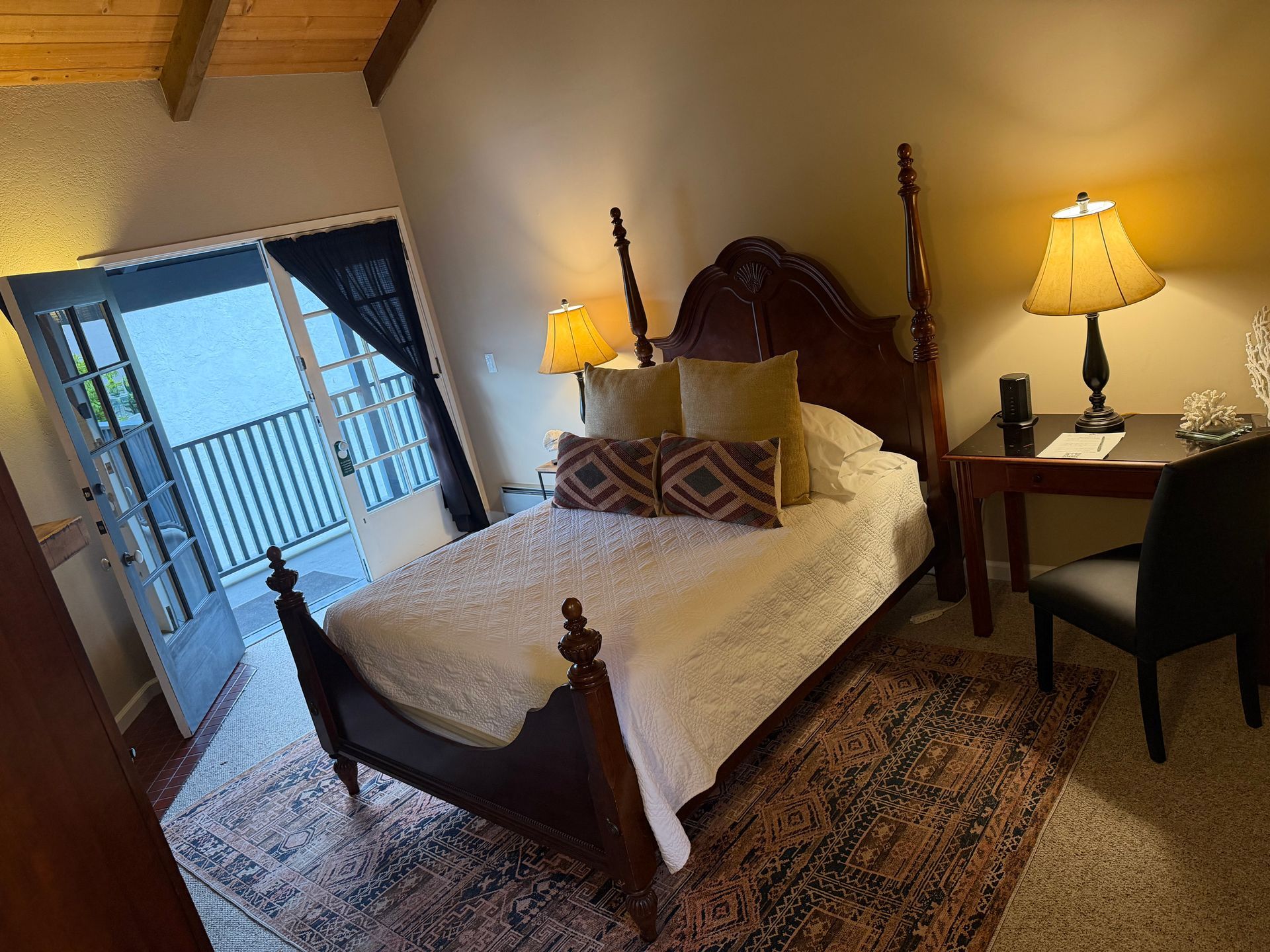 Bedroom with a bed, nightstand, and balcony door. Warm lighting. Antique-style furniture.