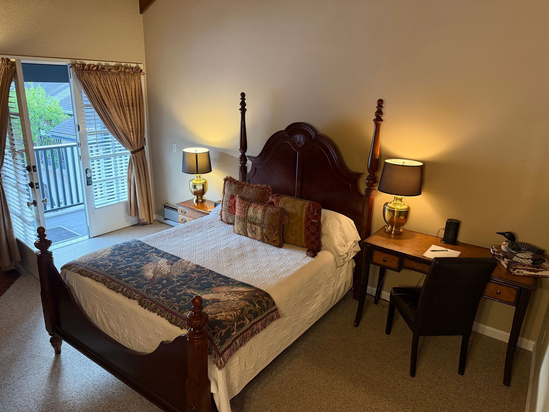 Bedroom with a four-poster bed, nightstands with lamps, a desk, and a balcony door.