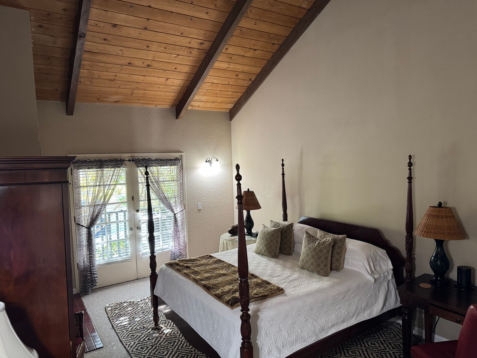 Bedroom with four-poster bed, wood ceiling, rug, and French doors leading to a balcony.