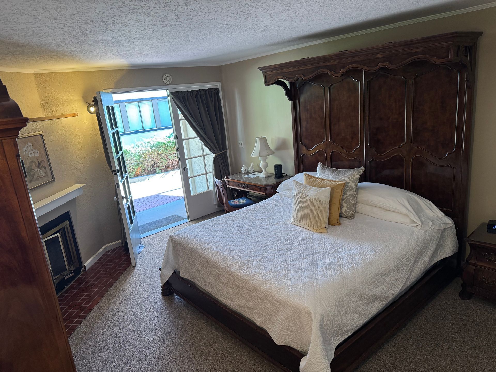 Bedroom with large wooden bed, fireplace, and open doors leading to a patio.