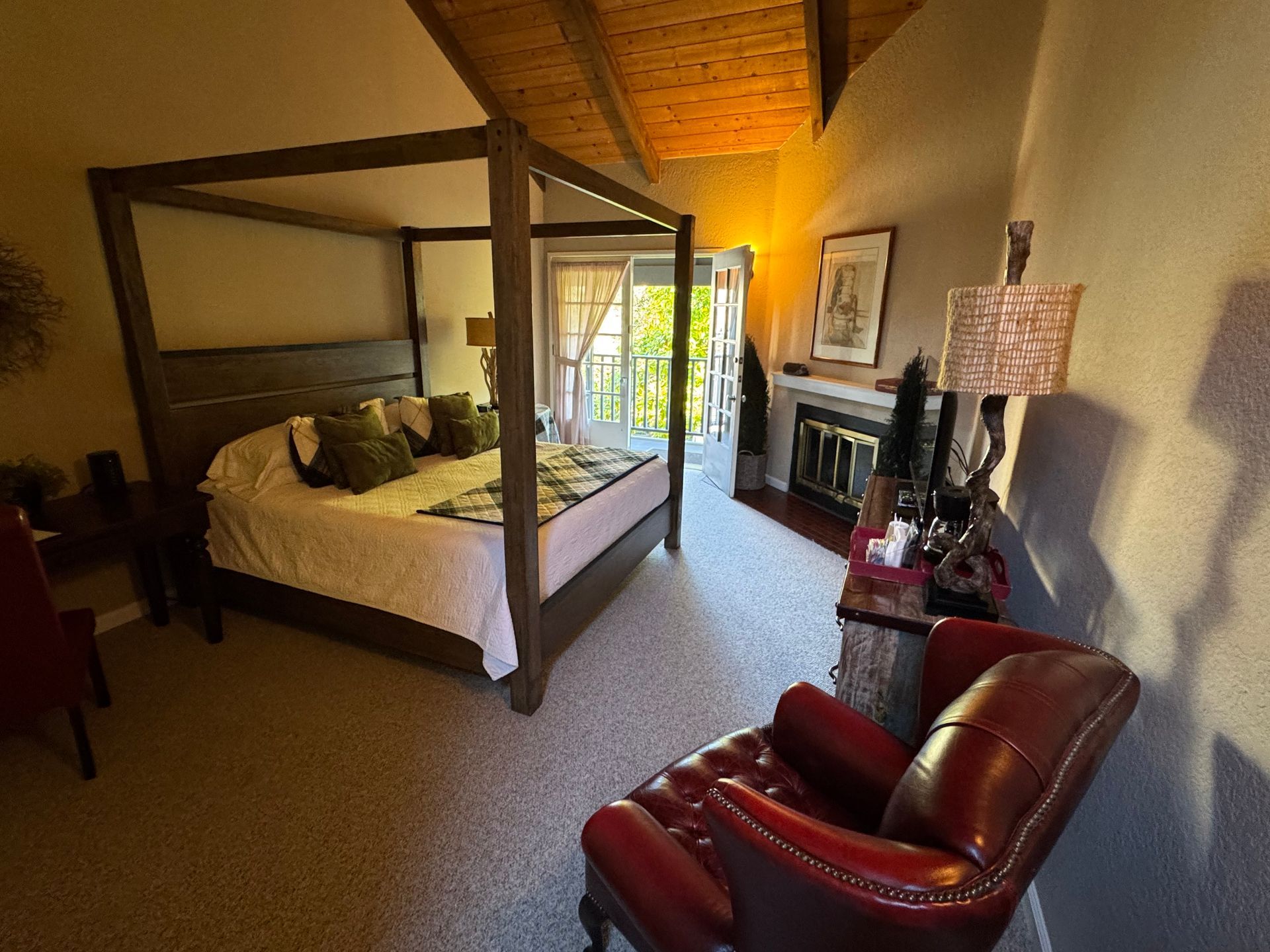 Bedroom with a four-poster bed, red leather armchair, fireplace, and balcony access.