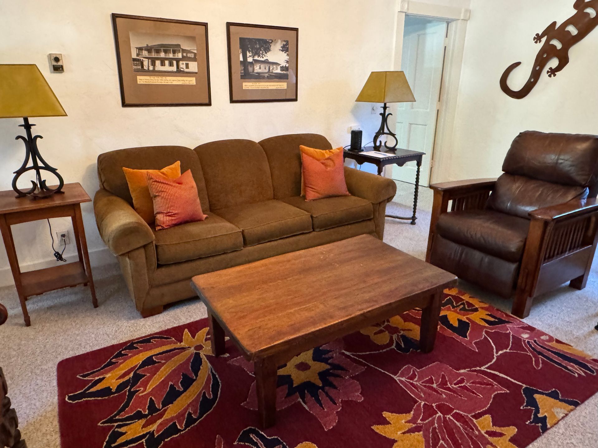 Living room with brown sofa, armchair, coffee table, rug, lamps, and wall art.