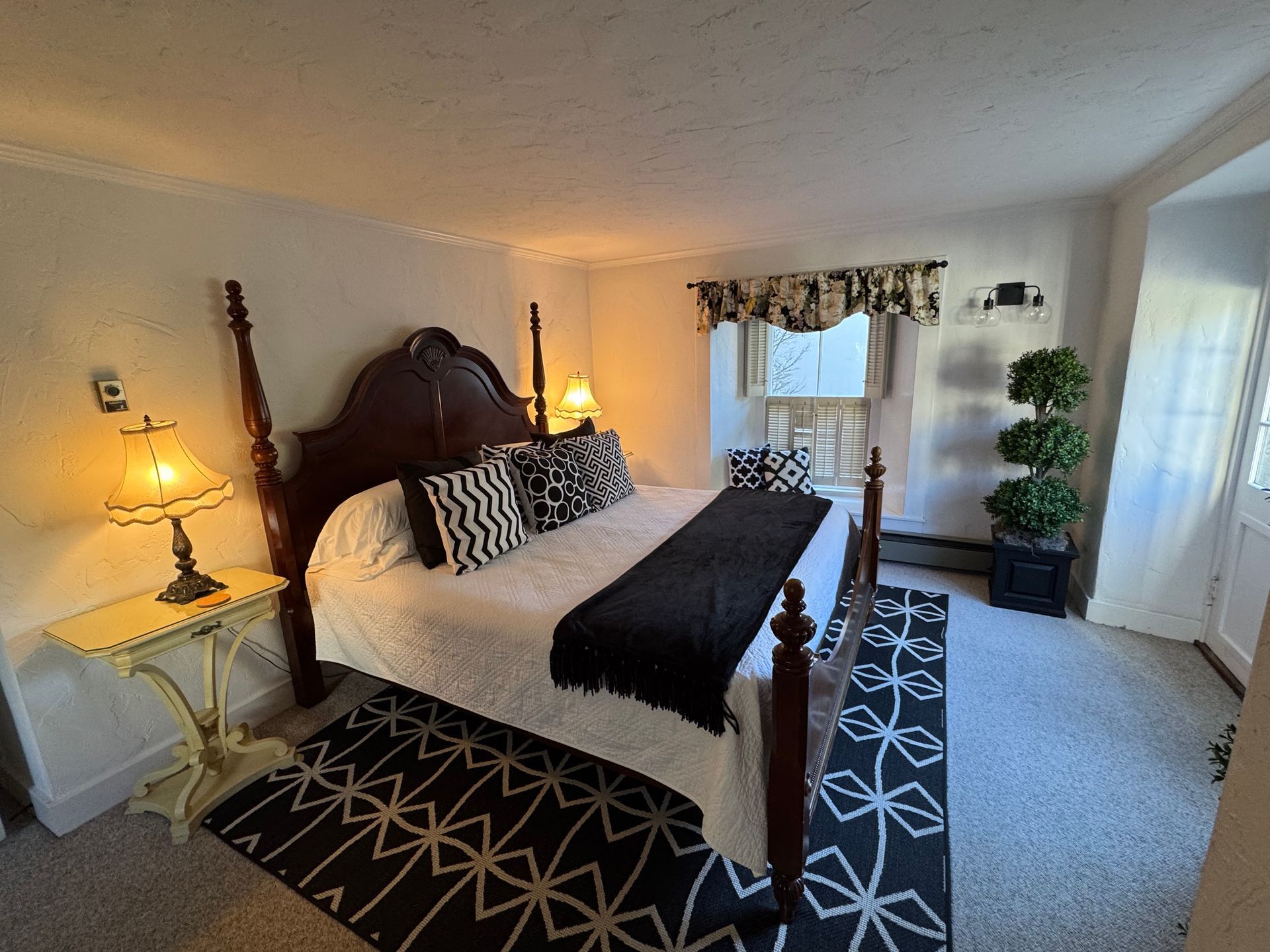 Bedroom with a dark wooden four-poster bed, black and white accents, and a small yellow side table with a lamp.