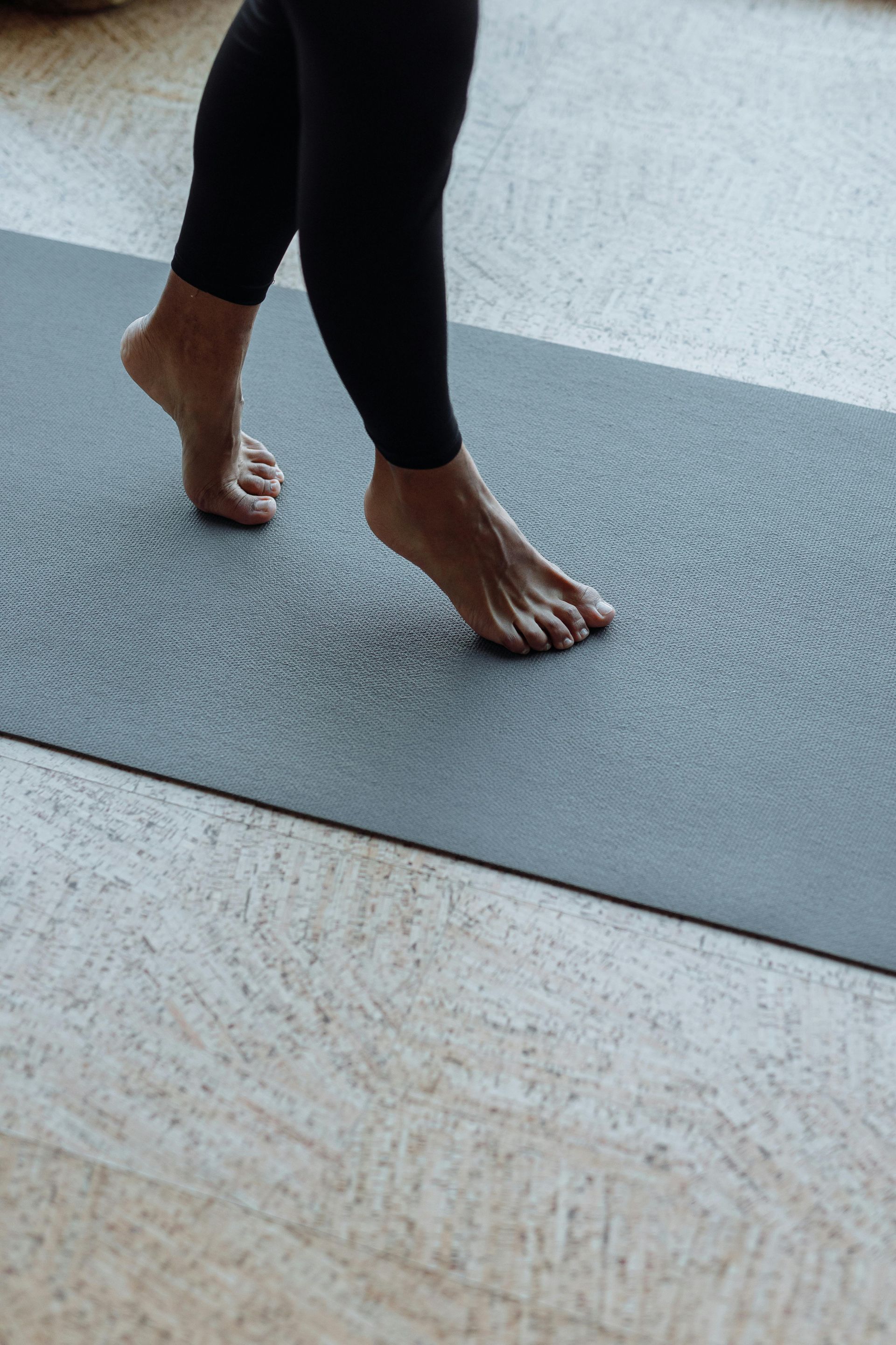 Pieds nus sur un tapis de yoga gris pendant une posture de yoga sur un sol clair