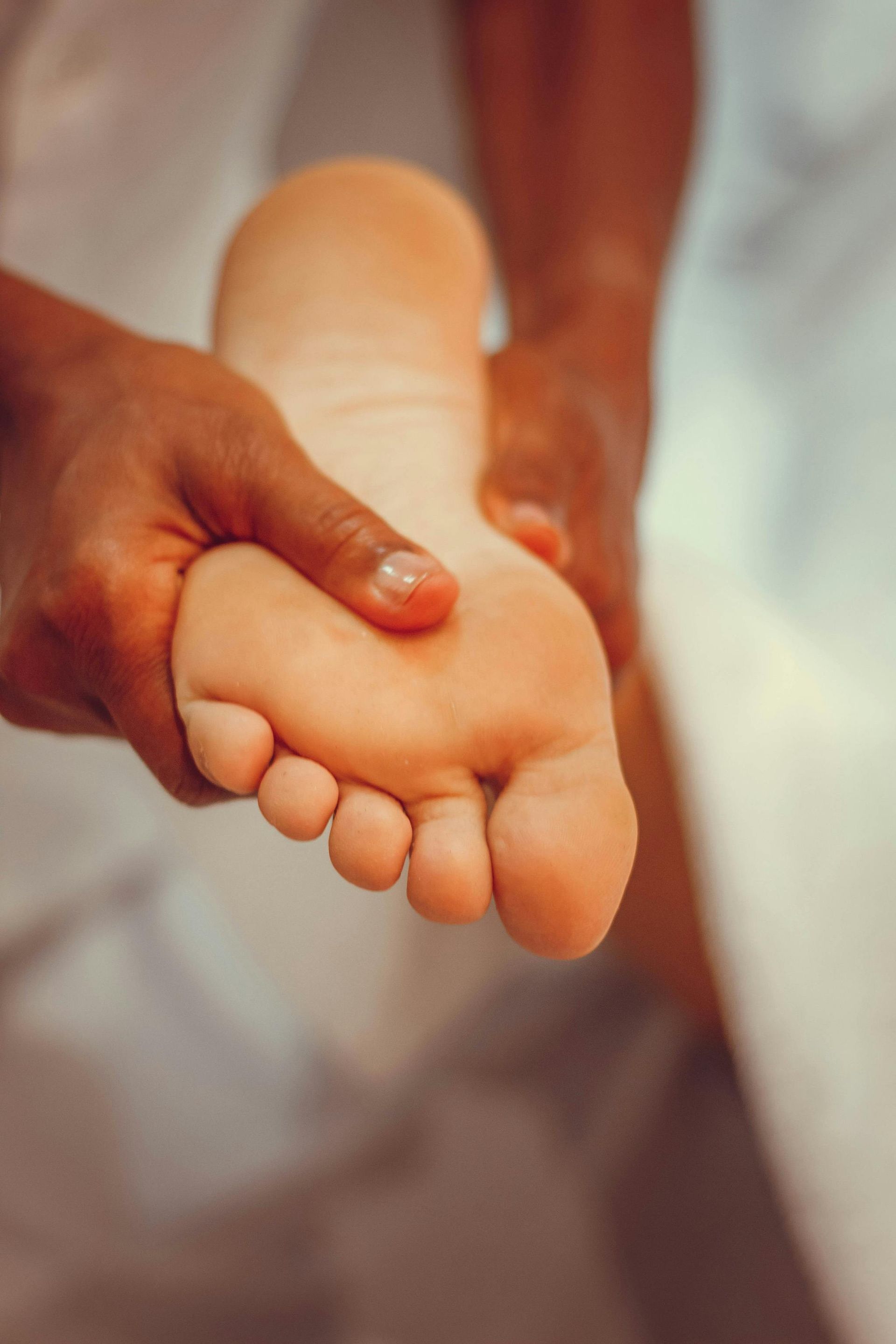 Un adulte tient le pied nu d'un bébé près de la caméra, la plante du pied tournée vers l'avant.