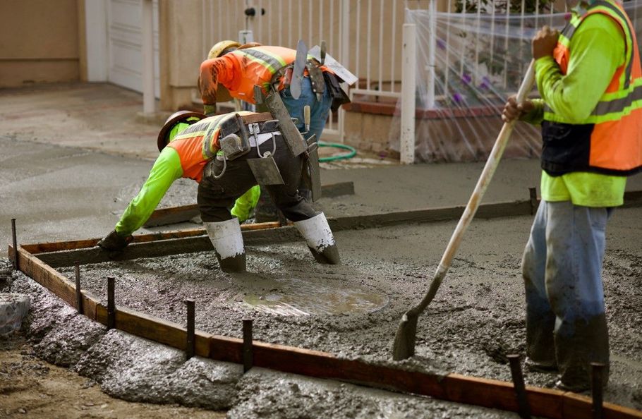 Construction workers pouring wet concrete on a job site, smoothing it with shovels and tools.