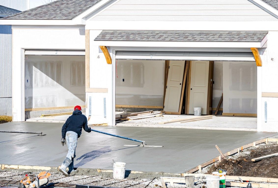 Worker spraying concrete in front of a new house with an open garage during construction
