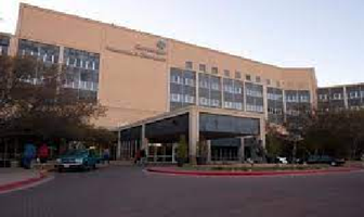 Exterior of a beige multi-story building with windows, a covered entrance, and parked cars at dusk