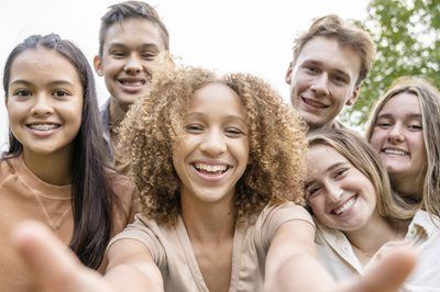 Smiling group taking a selfie outdoors, faces close to the camera.