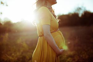 Pregnant person in a yellow dress standing outdoors in warm sunlight