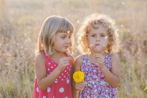 Two children in pink dresses standing in a field, holding yellow flowers
