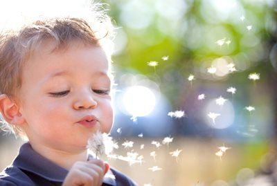 Child blowing on dandelion seeds with sparkling bokeh in the background