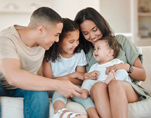 Family seated on a couch, smiling and gently holding a baby together