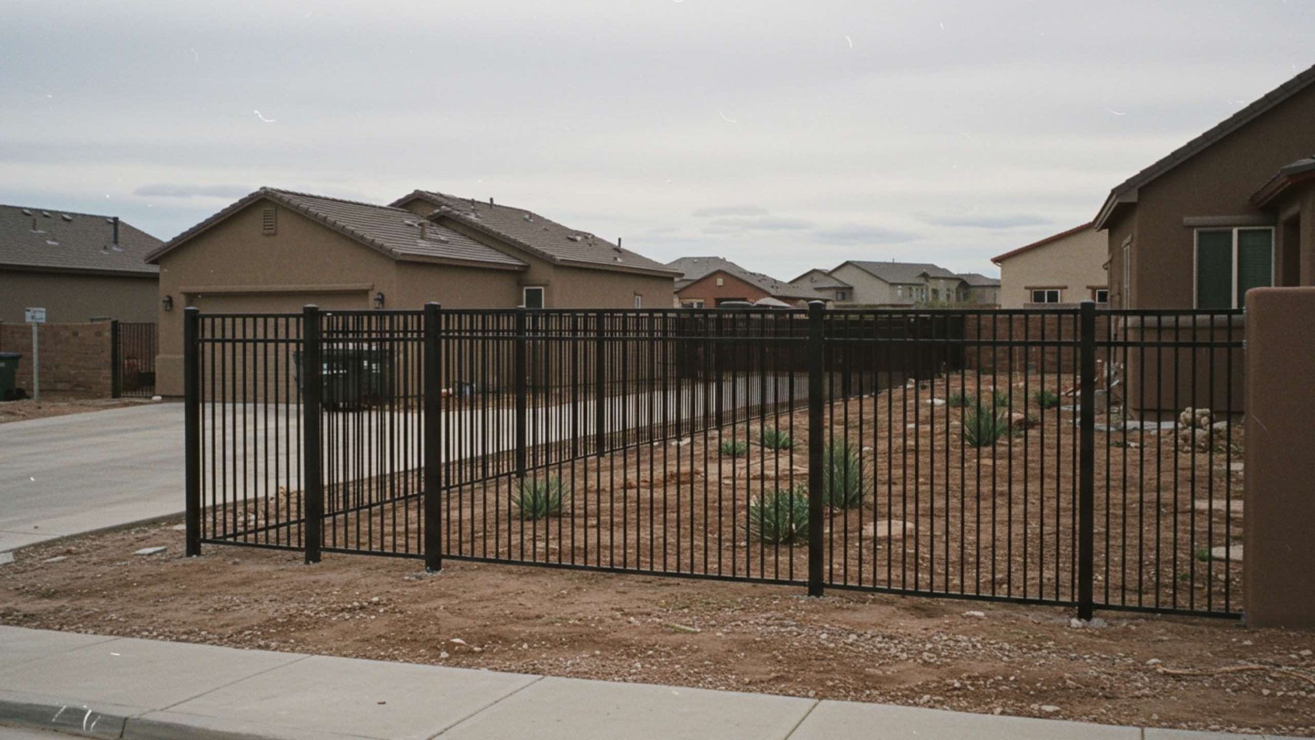 Black metal fence in front yard of a suburban home. Gravel and sparse vegetation in the yard.