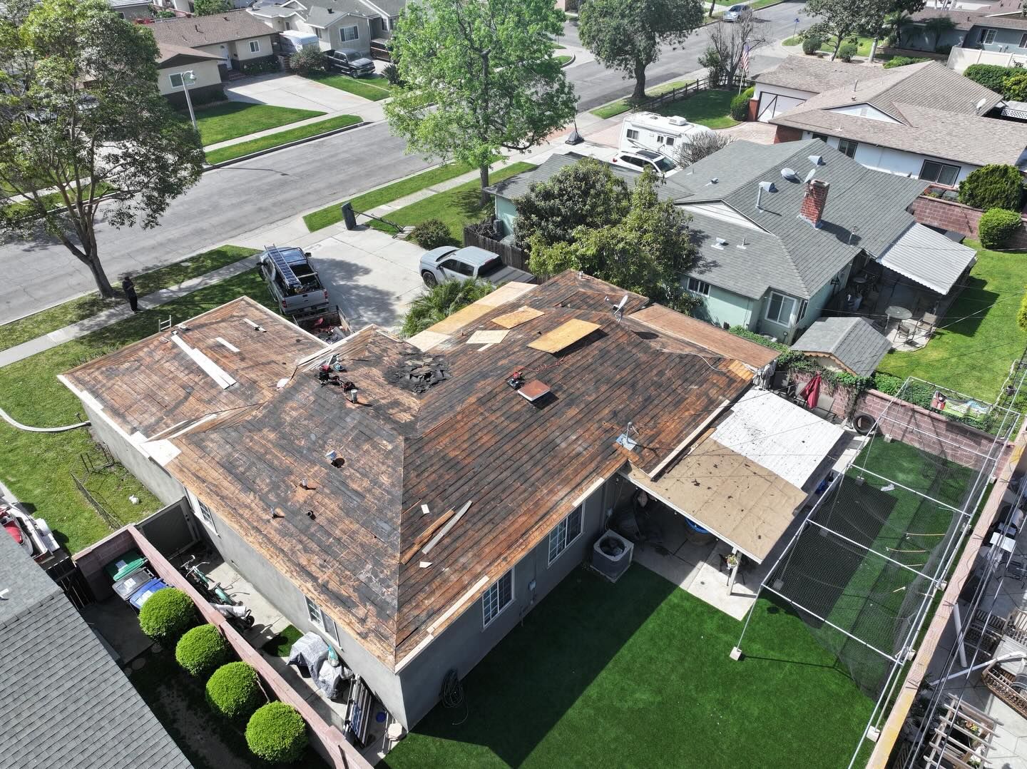 Aerial view of a residential home undergoing a roof replacement with exposed underlayment and patches of missing shingles.