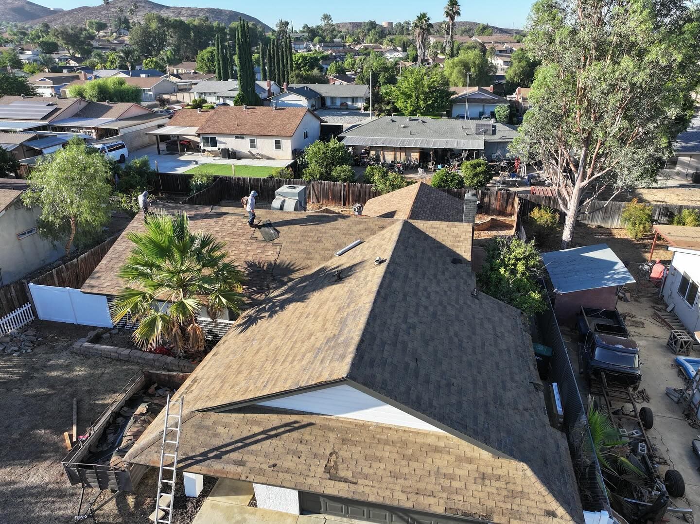 Aerial view of a residential house with a brown shingled roof being repaired by workers on a sunny day.