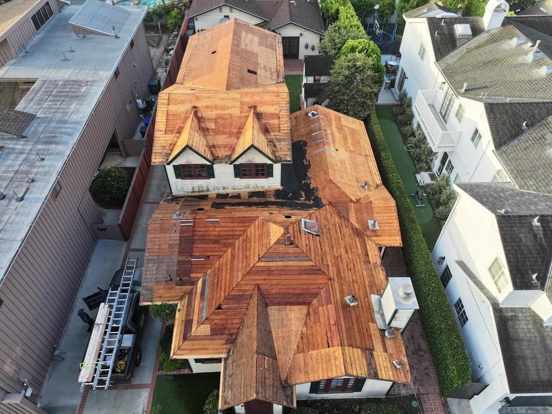 An aerial view of a residential home undergoing roof repairs, with exposed wood decking and a ladder on the side.